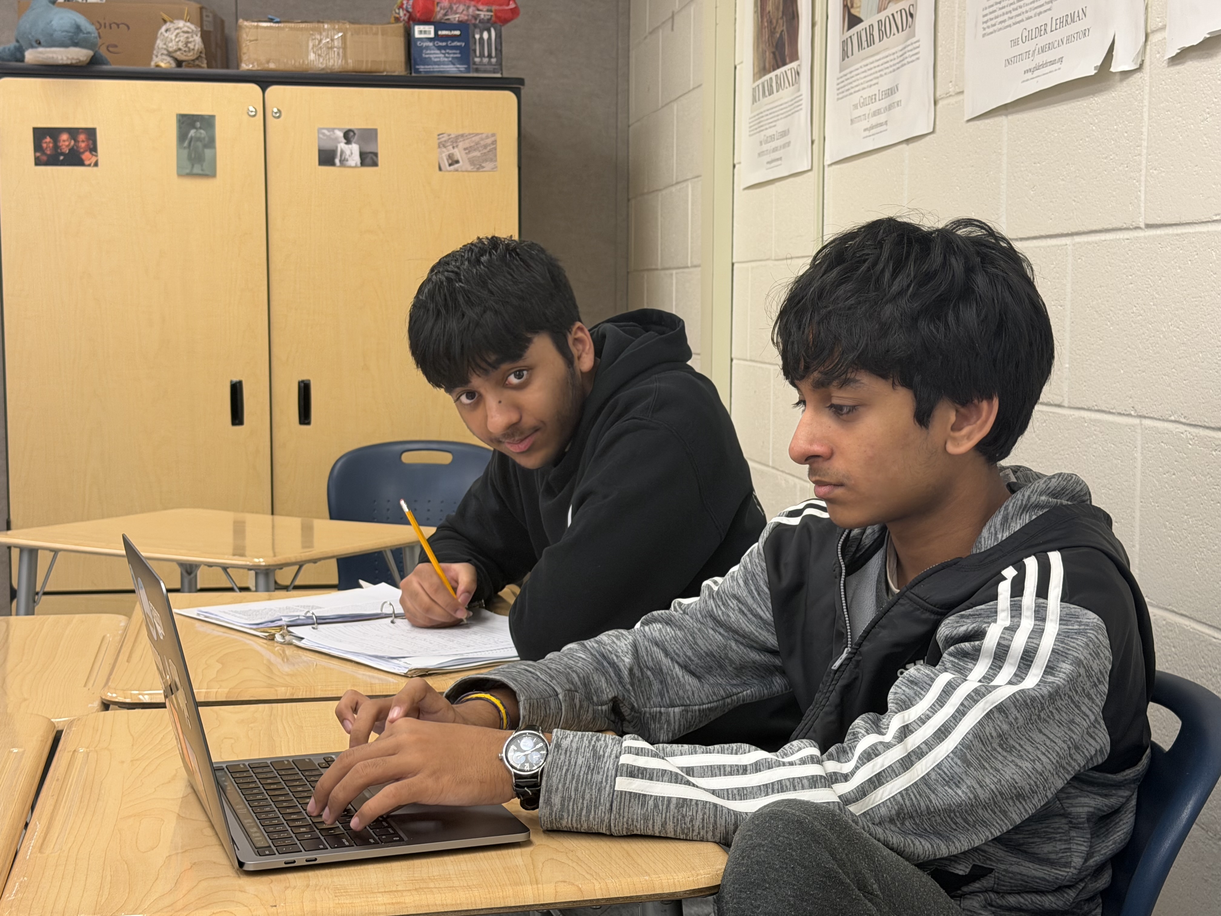 Two students working with a laptop and notebook